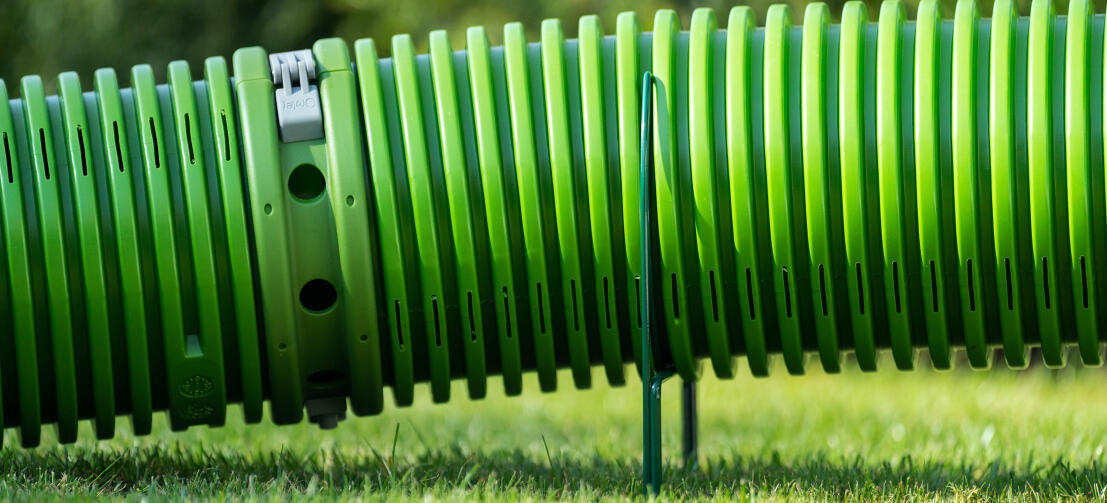 Zbliżenie zieloneGo tunelu Zippi podnoszoneGo z trawnika przez obręcze podpierające Zippi.
