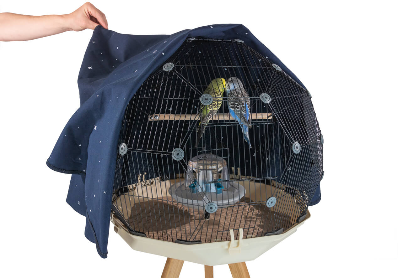 Dwie papużki faliste siedzą na żerdce w swojej Klatce dla Ptaków Geo z pokrywą na noc zdjętą do połowy